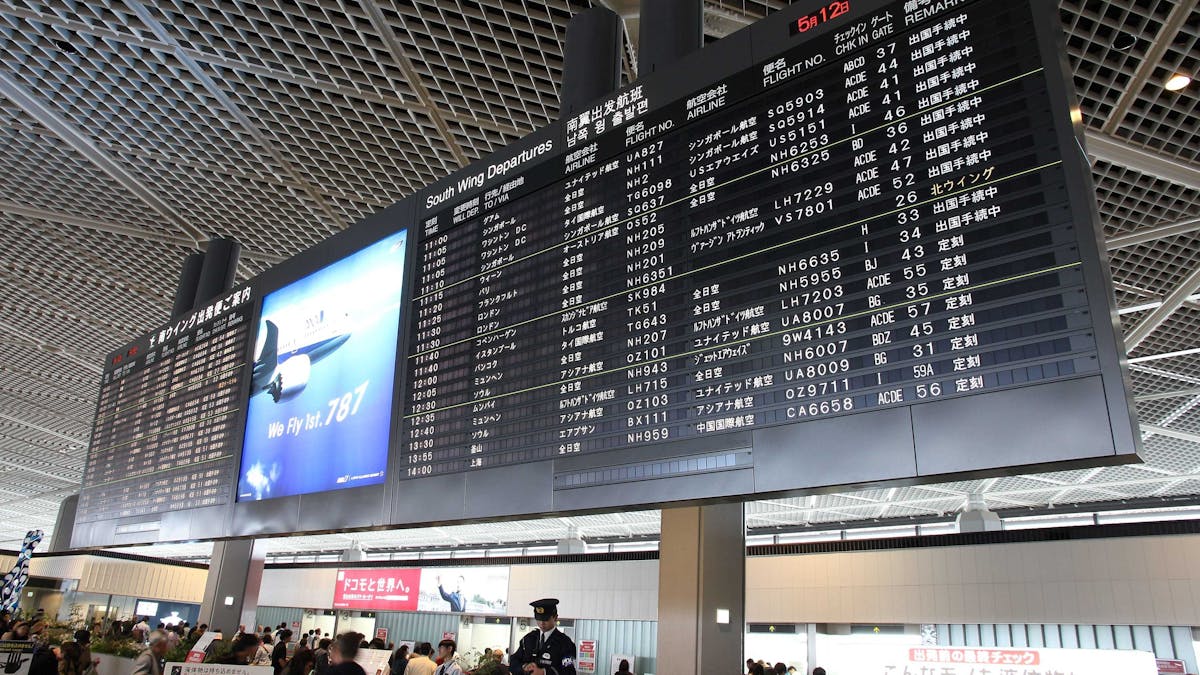 Passengers gathered around a Flight Information Display System at Narita Airport, attentively checking real-time updates on flight arrivals, departures, and gate numbers.