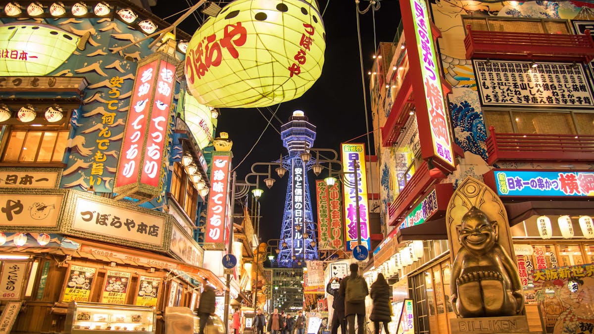 View of Tsuruhashi Fugetsu Shinsekai in Osaka, showcasing vibrant buildings adorned with colorful lights and electronic signage, surrounded by a bustling market atmosphere.