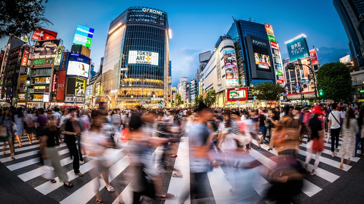 Crowds of people traverse the bustling Shibuya Crossing in Tokyo, with the evening sky and illuminated city buildings providing a captivating backdrop.